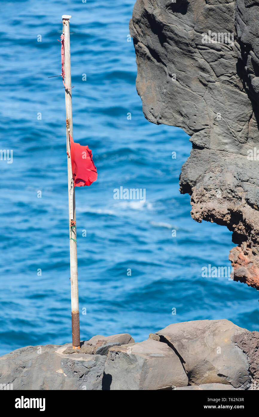 Red flag on a cliff in the surf near Playa de Nogales beach in La Palma, Spain. Stock Photo