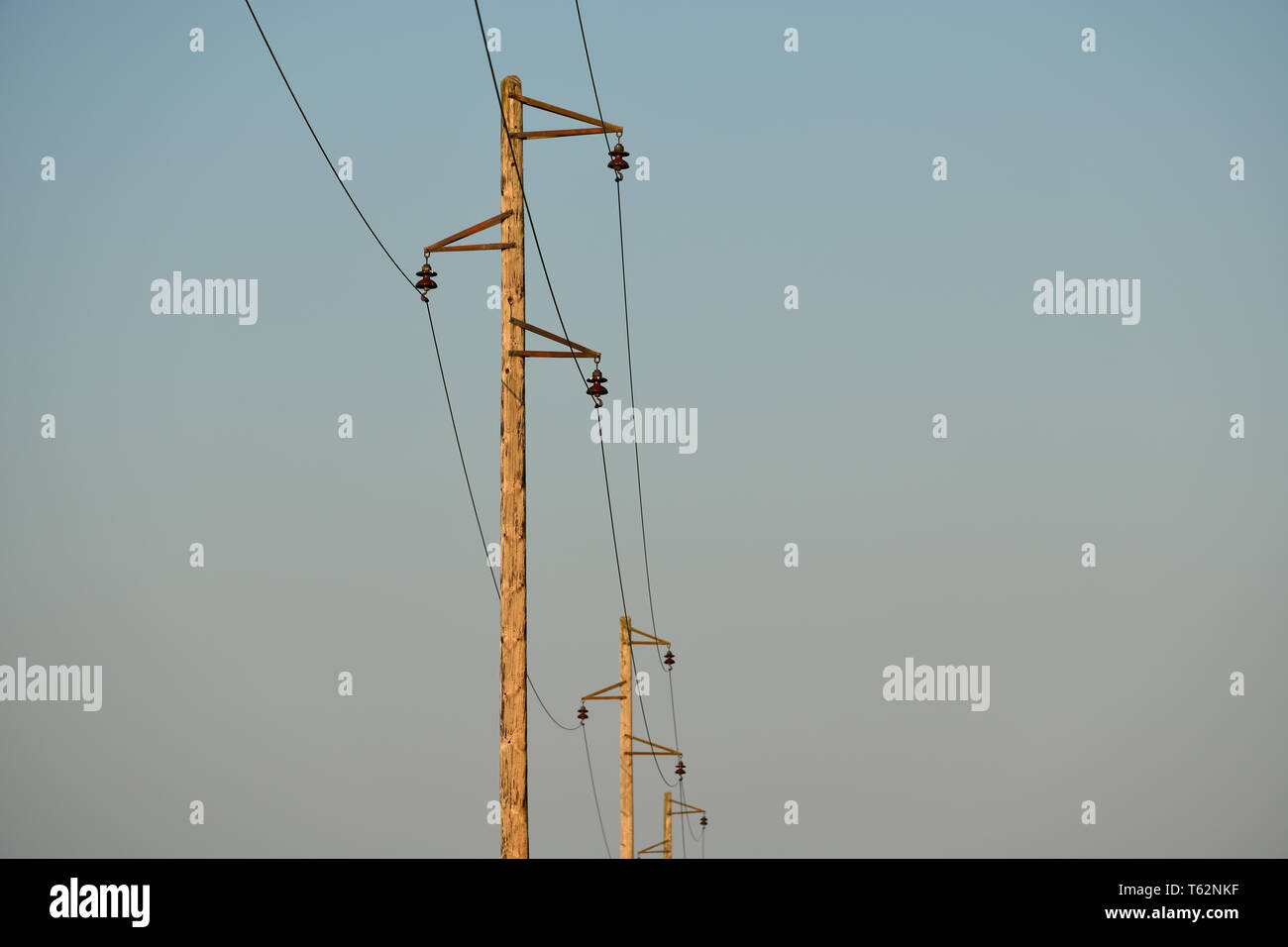 Electric pole and wires. An old overhead power line and single wood utility pole structure. Electrical power transmission and distribution cables. Stock Photo