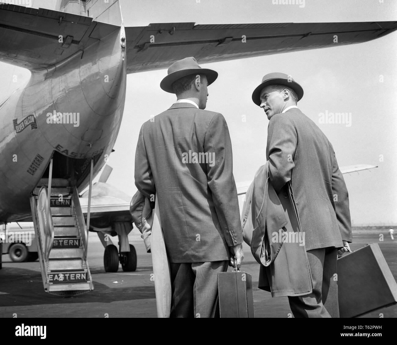 1950s TWO BUSINESSMEN TALKING ON TARMAC ABOUT TO ENTER REAR DOORS OF EASTERN AIRLINES PASSENGER PLANE  - a3124 DEB001 HARS MALES CORPORATE EXECUTIVES TRANSPORTATION B&W SELLING AIRPLANES EASTERN TRIP TARMAC REAR VIEW AIRLINES AVIATION TRAVELING BOSSES DEB001 BACK VIEW COMMERCIAL AVIATION ENTER MANAGERS MID-ADULT MID-ADULT MAN SALESMEN TRAVELER TRAVELERS APPROACHING BLACK AND WHITE CAUCASIAN ETHNICITY OLD FASHIONED Stock Photo