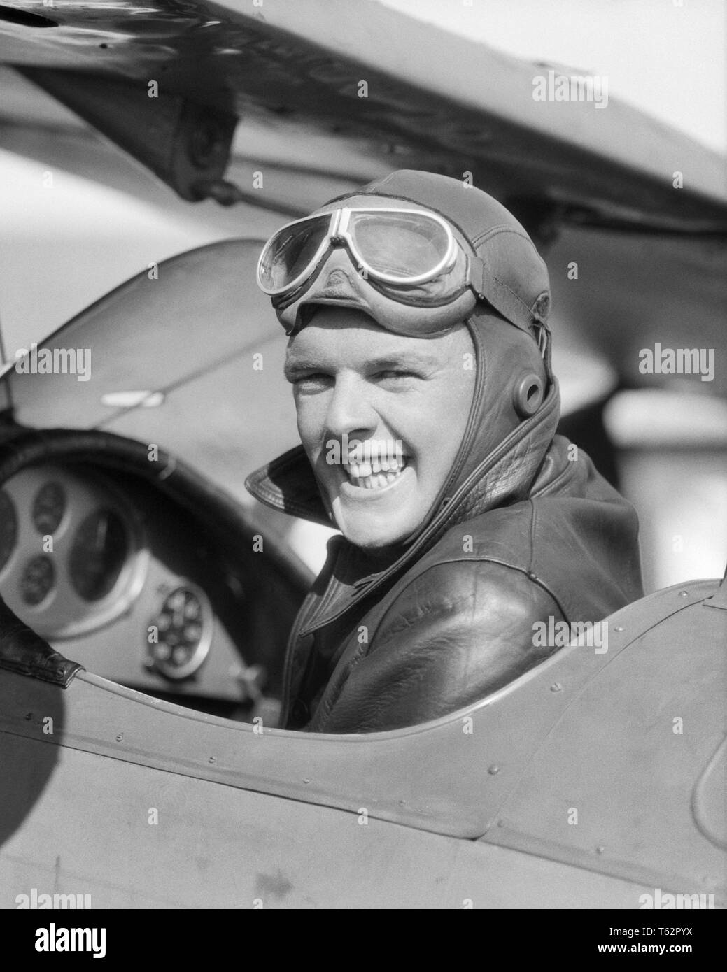 1930s MAN PILOT SITTING IN OPEN AIR COCKPIT SMILING LOOKING OVER HIS SHOULDER  - a4425 HAR001 HARS WELCOME PLEASED JOY LIFESTYLE PLANES JOBS PERSONS GOGGLES MALES TRANSPORTATION EXPRESSIONS B&W EYE CONTACT SKILL OCCUPATION HAPPINESS SKILLS HEAD AND SHOULDERS CHEERFUL ADVENTURE AIRPLANES HIS EXCITEMENT AUTHORITY AVIATION OCCUPATIONS SMILES COCKPIT AVIATOR JOYFUL MID-ADULT MID-ADULT MAN BIPLANE BLACK AND WHITE BRAVE CAUCASIAN ETHNICITY HAR001 OLD FASHIONED Stock Photo