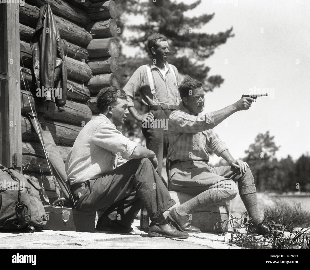 1930s THREE MEN TOGETHER OUTSIDE NORTH WOODS HUNTING FISHING LOG CABIN SEATED MAN AIMING PLINKING WITH COLT 22 CALIBER PISTOL - a5530 HAR001 HARS EXTERIOR KNOWLEDGE LEADERSHIP RECREATION DIRECTION CONNECTION STYLISH OUTDOORSMAN SPORTSMEN AIMING COLT COOPERATION FIREARM FIREARMS MID-ADULT MID-ADULT MAN PISTOL TOGETHERNESS 22 CALIBER BLACK AND WHITE CAUCASIAN ETHNICITY HAR001 OLD FASHIONED Stock Photo