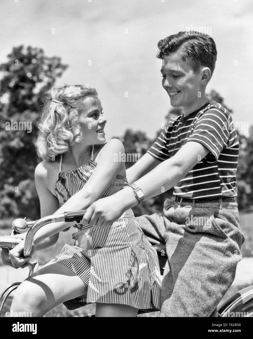 1930s 1940s SMILING TEENAGE BOY AND GIRL RIDING BICYCLE TOGETHER  - b1053 HAR001 HARS BALANCE PLEASED JOY LIFESTYLE FEMALES RURAL HEALTHINESS FRIENDSHIP HALF-LENGTH ADOLESCENT PERSONS CARING MALES TEENAGE GIRL TEENAGE BOY CONFIDENCE B&W HAPPINESS CHEERFUL RECREATION OPPORTUNITY SMILES CONNECTION JOYFUL STYLISH TEENAGED AFFECTION GROWTH JUVENILES MEETS TOGETHERNESS BLACK AND WHITE CAUCASIAN ETHNICITY HAR001 OLD FASHIONED Stock Photo