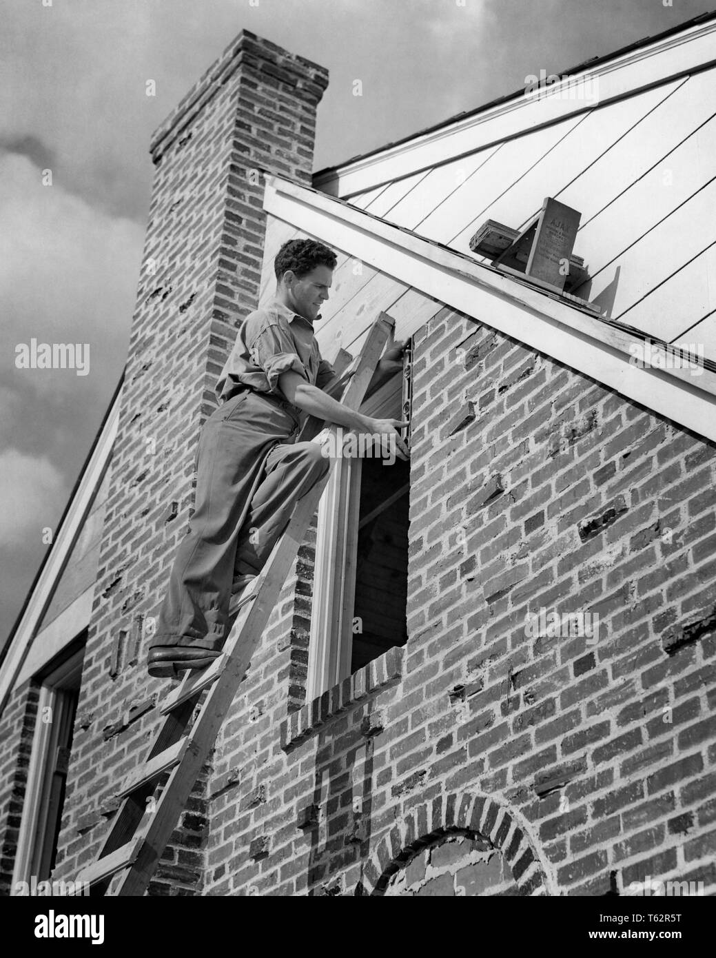 1940s WORKMAN ON STEPLADDER FITTING A NEW WINDOW ON BRICK HOUSE - b11694 HAR001 HARS RESIDENTIAL MALES RISK BUILDINGS PROFESSION CONFIDENCE B&W SKILL OCCUPATION SKILLS PROPERTY STRENGTH CAREERS EXTERIOR FITTING KNOWLEDGE LABOR EMPLOYMENT HOMES OCCUPATIONS REAL ESTATE CONCEPTUAL STRUCTURES RESIDENCE EDIFICE EMPLOYEE STEPLADDER YOUNG ADULT MAN BLACK AND WHITE CAUCASIAN ETHNICITY HAR001 INSTALLING LABORING OLD FASHIONED Stock Photo