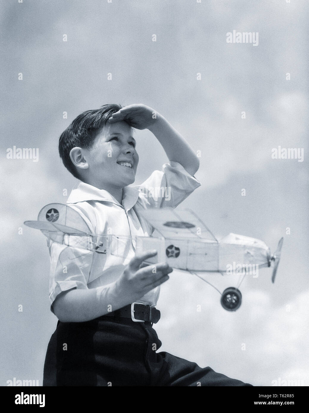 1930s SMILING YOUNG BOY SHADING EYES WITH HAND LOOKING SKYWARD HOLDING  RUBBER BAND WINDUP BALSA WOOD TISSUE PAPER MODEL AIRPLANE - b11981 HAR001  HARS PLANES FLIGHT RURAL COPY SPACE HALF-LENGTH INSPIRATION MALES