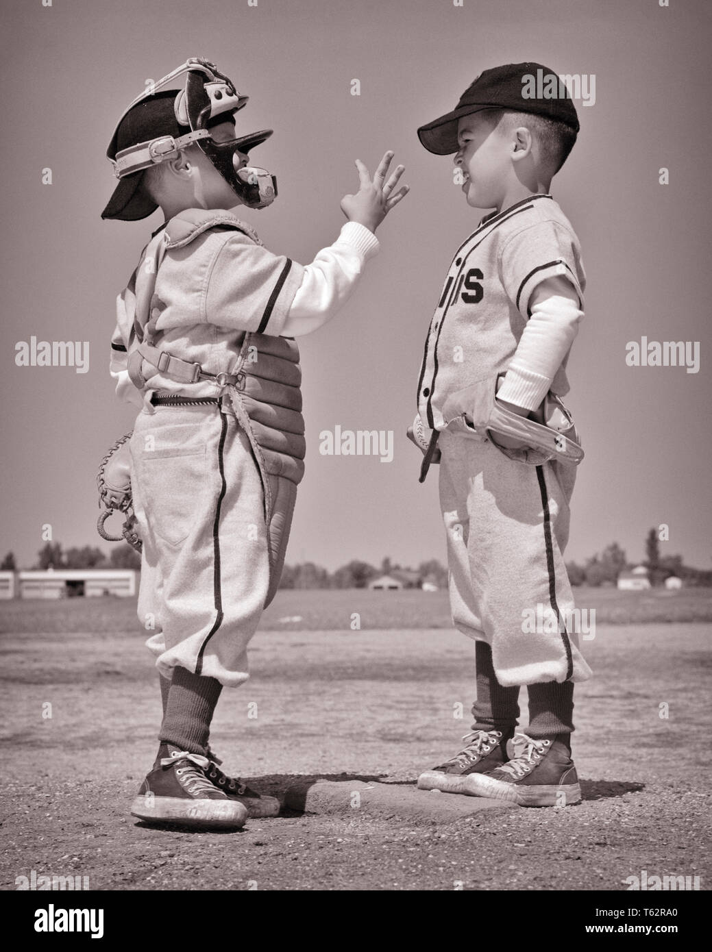 1960s TWO BOYS PITCHER AND CATCHER IN LITTLE LEague baseball uniforms having a conversation on the pitcher’s mound  - b14306 HAR001 HARS B&W PITCHER CATCHER RECREATION MOUND DIRECTION ON THE ATHLETES BALL GAME BALL SPORT COOPERATION GROWTH JUVENILES TOGETHERNESS BASEBALL BAT BLACK AND WHITE CAUCASIAN ETHNICITY HAR001 OLD FASHIONED Stock Photo
