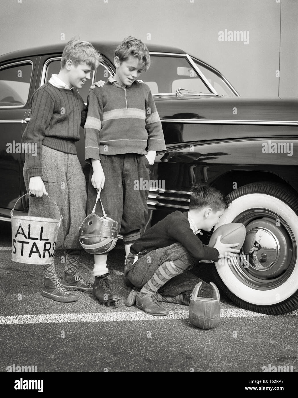 1940s THREE PRETEEN BOYS FOOTBALL PLAYERS WEARING KNICKERBOCKERS FILLING BALL WITH AIR SWIPED FROM AUTOMOBILE WHITEWALL TIRE - b13555 HAR001 HARS TEAMWORK ATHLETE KNICKERS LIFESTYLE BROTHERS TIRE WOOL COPY SPACE FULL-LENGTH HALF-LENGTH INSPIRATION AUTOMOBILE MALES RISK ATHLETIC SIBLINGS TRANSPORTATION PLAYERS STEALING B&W SUCCESS TEMPTATION ADVENTURE FILLING STYLES TROUSERS STRATEGY AUTOS WHITEWALL RECREATION INNOVATION OPPORTUNITY PRETEEN SIBLING AUTOMOBILES IMAGINATION STYLISH VEHICLES INFLATING KNICKERBOCKERS CREATIVITY FASHIONS IDEAS JUVENILES PRE-TEEN PRE-TEEN BOY TOGETHERNESS Stock Photo