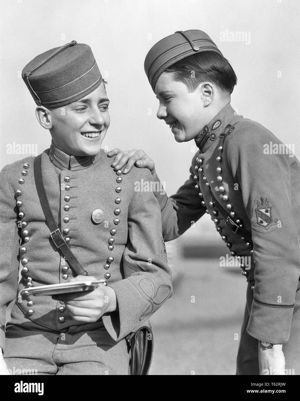 1920s TWO SMILING BOYS HOTEL BELLHOPS WEARING TRADITIONAL BRASS BUTTON UNIFORMS AND BELLBOY ROUND BRIMLESS CAPS TALKING TOGETHER - b3646 HAR001 HARS BUSY NOSTALGIA INDUSTRY OLD FASHION 1 JUVENILE COMMUNICATION CAREER ROUND INFORMATION PLEASED JOY LIFESTYLE JOBS LUXURY FRIENDSHIP HALF-LENGTH PERSONS TRADITIONAL MALES TEENAGE BOY PROFESSION B&W SKILL OCCUPATION SKILLS CHEERFUL CUSTOMER SERVICE AND CAREERS PRIDE IN OCCUPATIONS SMILES UNIFORMS CONCEPTUAL CAPS JOYFUL STYLISH TEENAGED BELLMAN BELLBOY BRASS BUTTON JUVENILES PRE-TEEN PRE-TEEN BOY BLACK AND WHITE CAUCASIAN ETHNICITY HAR001 Stock Photo