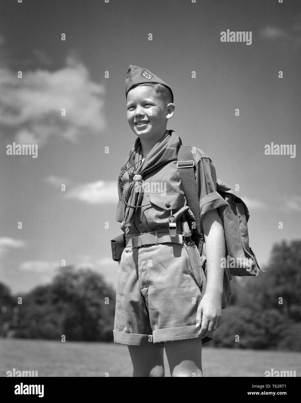 1950s SMILING YOUNG TEENAGE BOY SCOUT STANDING AT ATTENTION WEARING UNIFORM CAP SHIRT NECKERCHIEF SHORTS PACK WHISTLE OUTDOORS - b6044 HAR001 HARS JUVENILE FACIAL STYLE SAFETY PLEASED JOY LIFESTYLE SATISFACTION SCOUT PACK RURAL HEALTHINESS COPY SPACE HALF-LENGTH PERSONS INSPIRATION SCOUTS MALES TEENAGE BOY EXPRESSIONS B&W SUCCESS HAPPINESS CHEERFUL ADVENTURE STRENGTH COURAGE ATTENTION CHOICE KNOWLEDGE LEADERSHIP RECREATION PRIDE NECKERCHIEF AT SMILES BOY SCOUT THRIFTY CONCEPTUAL COURTEOUS FRIENDLY HELPFUL JOYFUL KIND REVERENT STYLISH TEENAGED TRUSTWORTHY COOPERATION CREATIVITY GROWTH JUVENILES Stock Photo