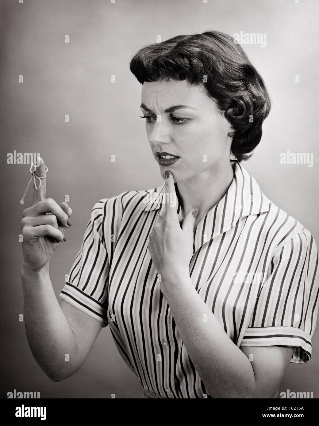 1950s FORGETFUL CONFUSED WOMAN HOUSEWIFE TRYING TO REMEMBER SOMETHING LOOKING AT REMINDER STRING TIED ON FINGER - bx016692 CAM001 HARS B&W PUZZLED SADNESS HOMEMAKER THOUGHT FORGET HOMEMAKERS STRATEGY FORGETFUL IDEA REMEMBER TRYING THINK CAM001 AT ON TO HOUSEWIVES PONDERING REMINDER CONNECTION CONCEPTUAL FORGOTTEN REMEMBERING SOMETHING FAILURE FORGETTING IDEAS MID-ADULT MID-ADULT WOMAN SOLUTIONS TECHNIQUE BLACK AND WHITE CAUCASIAN ETHNICITY FAIL OLD FASHIONED Stock Photo