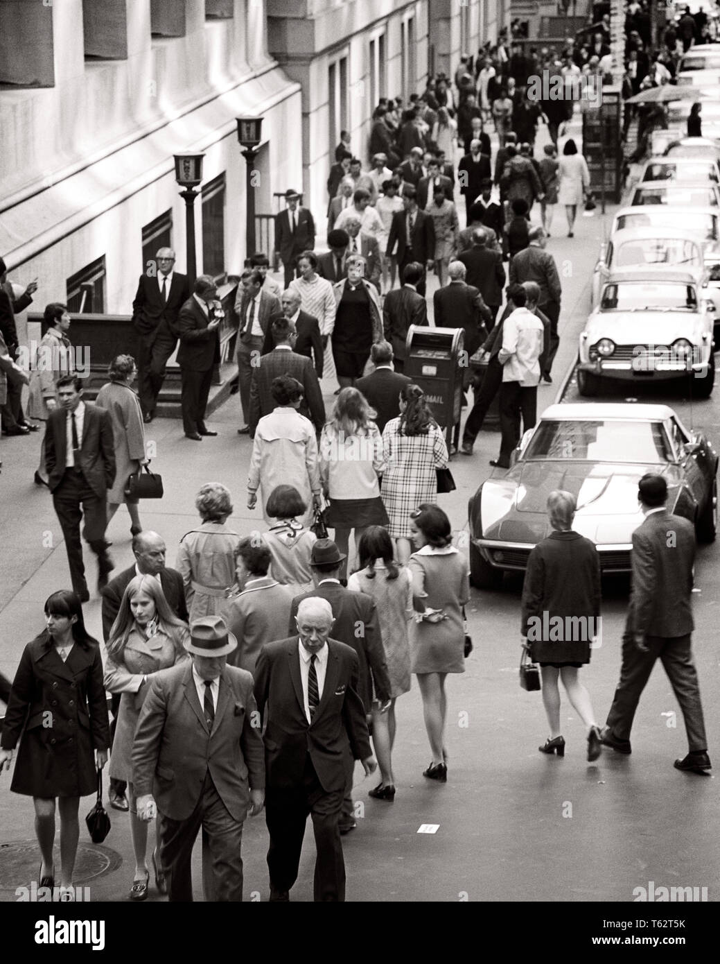 1970s CITY STREET FULL OF MEN AND WOMEN WORKERS  WALKING  CROSSING THE STREET COMMUTING - c10918 HAR001 HARS PEDESTRIANS TRANSPORTATION B&W GATHERING HIGH ANGLE AND AUTOS CONGESTED COMMUTING OCCUPATIONS AUTOMOBILES VEHICLES COOPERATION THRONG BLACK AND WHITE CAUCASIAN ETHNICITY HAR001 OLD FASHIONED Stock Photo