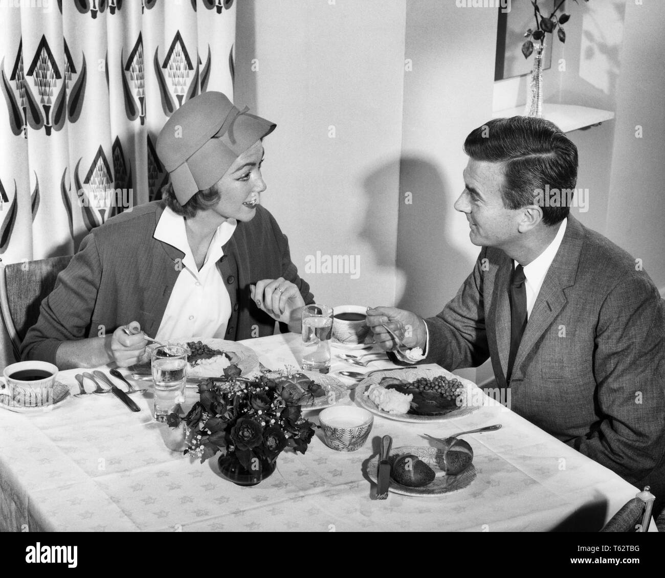 1950s SMILING COUPLE EATING DINNER IN RESTAURANT WOMAN WEARING HAT MAN SUIT AND TIE - d1498 HAR001 HARS OLD TIME BUSY NOSTALGIA OLD FASHION STYLE COMMUNICATION YOUNG ADULT PLEASED JOY LIFESTYLE FEMALES MARRIED SPOUSE HUSBANDS FRIENDSHIP HALF-LENGTH LADIES PERSONS CARING MALES B&W PARTNER DATING SUIT AND TIE HAPPINESS CHEERFUL STRATEGY EXCITEMENT RECREATION IN OPPORTUNITY SMILES SUPPER CONNECTION COURTSHIP CONCEPTUAL JOYFUL STYLISH SEXUALLY POSSIBILITY PROSPECTIVE RELAXATION ROMANTICALLY SOCIALLY TOGETHERNESS WIVES YOUNG ADULT MAN YOUNG ADULT WOMAN BLACK AND WHITE CAUCASIAN ETHNICITY HAR001 Stock Photo