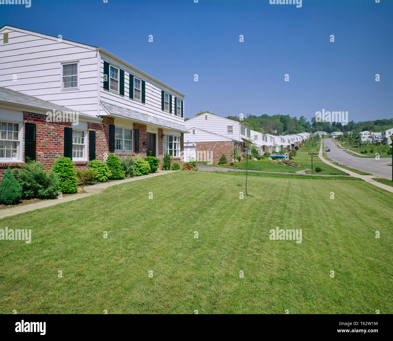 1970s SUBURBAN BRICK AND CLAPBOARD HOUSE WITH FRESH GREEN GRASS FRONT