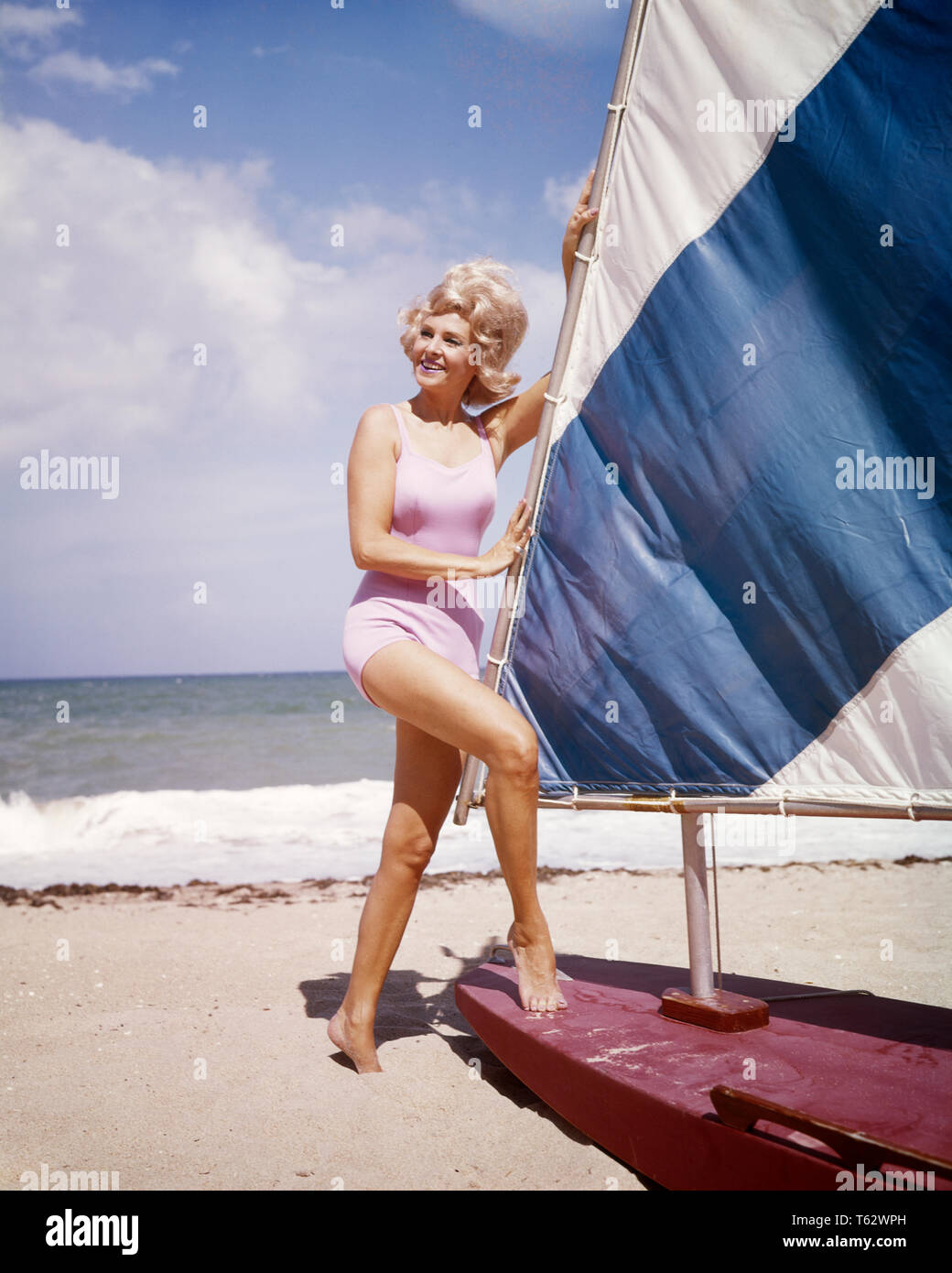 1960s MIDDLE AGED WOMAN WITH BLOND WIND BLOWN BIG HAIR WEARING PINK ONE PIECE BATHING SUIT STANDING BY SAIL BOAT ON OCEAN BEACH - kg2694 SCH002 HARS SAIL CHEERFUL BY ON SMILES CONCEPTUAL BLOWN JOYFUL SAIL BOAT MIDDLE AGE BATHING SUIT MID-ADULT MID-ADULT WOMAN BIG HAIR CAUCASIAN ETHNICITY OLD FASHIONED ONE PIECE WIND BLOWN Stock Photo