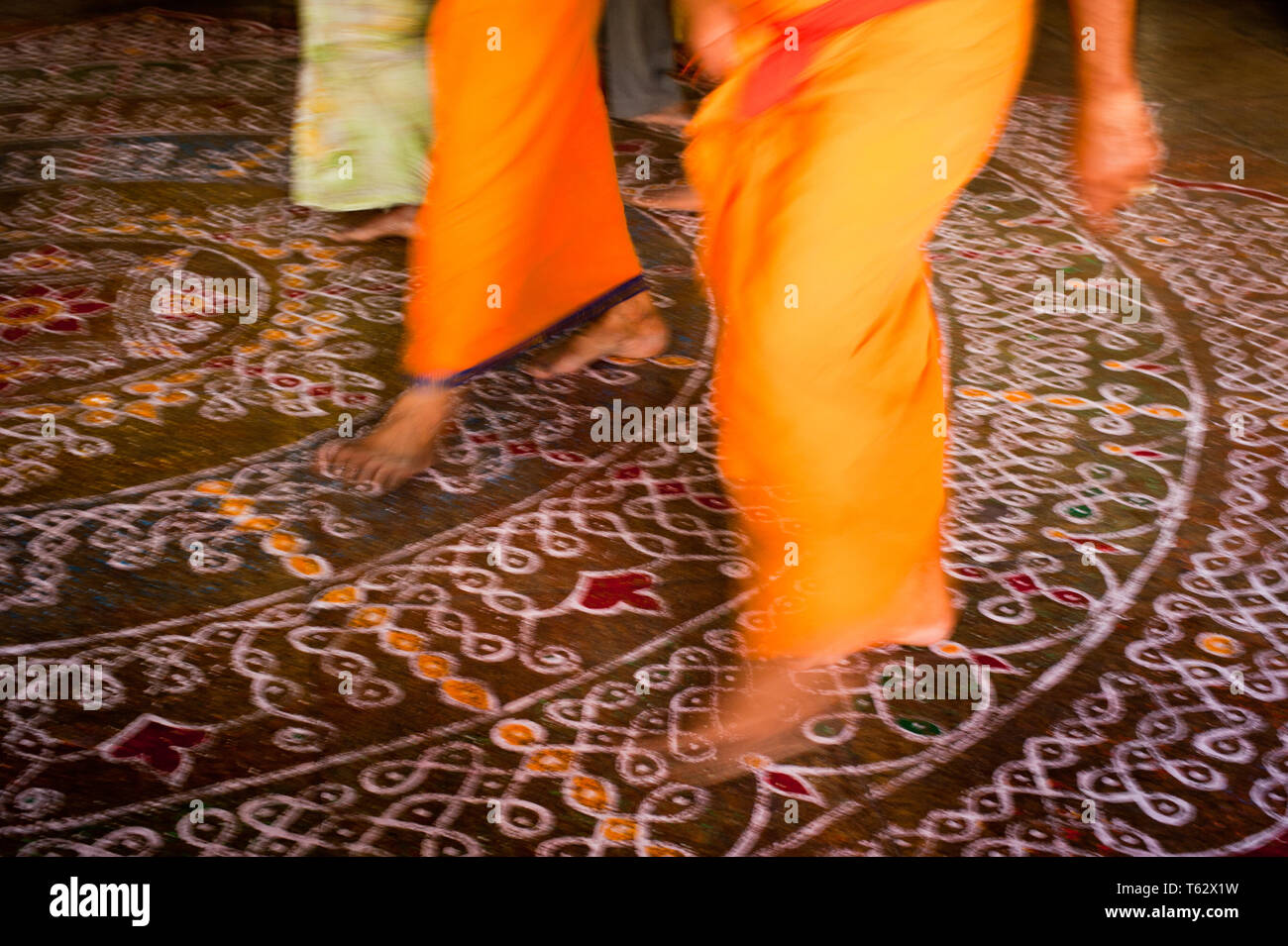 Abstract image of motion blurred barefoot pilgrim people in colorful clothes walking on the floor with painted mandala ornament. Traditional decoratio Stock Photo