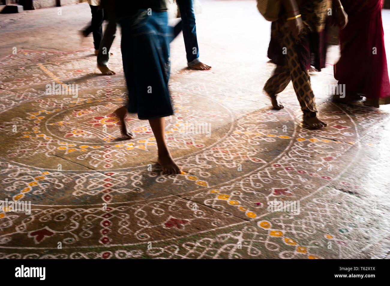 Abstract image of motion blurred barefoot pilgrim people in colorful clothes walking on the floor with painted mandala ornament. Traditional decoratio Stock Photo