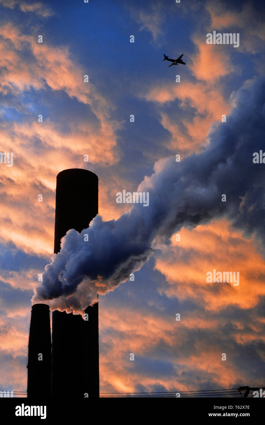 1990s AIRPLANE FLYING OVER SMOKESTACK EMITTING WATER VAPOR STEAM SMOKE AT SUNSET  - ki9417 LGA001 HARS INNOVATION AT CONCERN POLITICS CONCEPTUAL SUNRISE AVOIDING SYMBOLIC COMMERCIAL AVIATION OVERLOOKING SOLUTIONS SURVIVAL WATER VAPOR CLIMATE OLD FASHIONED REPRESENTATION SMOKESTACK Stock Photo