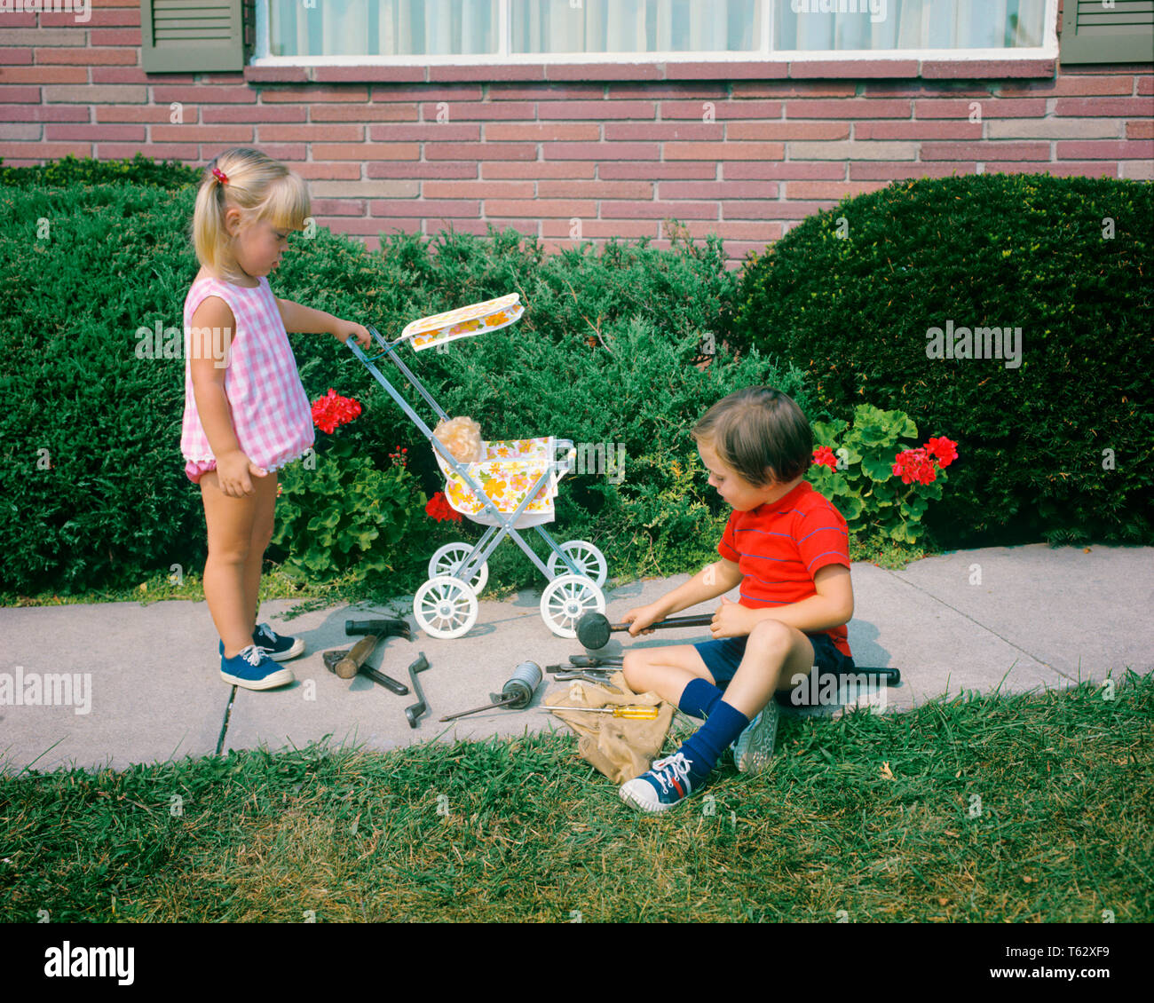 1970s LITTLE GIRL PUSHING TOY BABY CARRIAGE AND BOY PLAYING WITH TOOLS ON SIDEWALK GENDER SPECIFIC ROLE PLAY - kj5345 HAR001 HARS REPAIR STYLE COMMUNICATION TEAMWORK FEMALES BROTHERS HOME LIFE COPY SPACE FRIENDSHIP HALF-LENGTH CARING MALES ROLE SIBLINGS FIXING SISTERS CARRIAGE HIGH ANGLE AND ON OCCUPATIONS SIBLING REPAIRING FIX BABY DOLL COOPERATION GENDER JUVENILES TOGETHERNESS BABY CARRIAGE BEST FRIENDS CAUCASIAN ETHNICITY HAR001 OLD FASHIONED Stock Photo