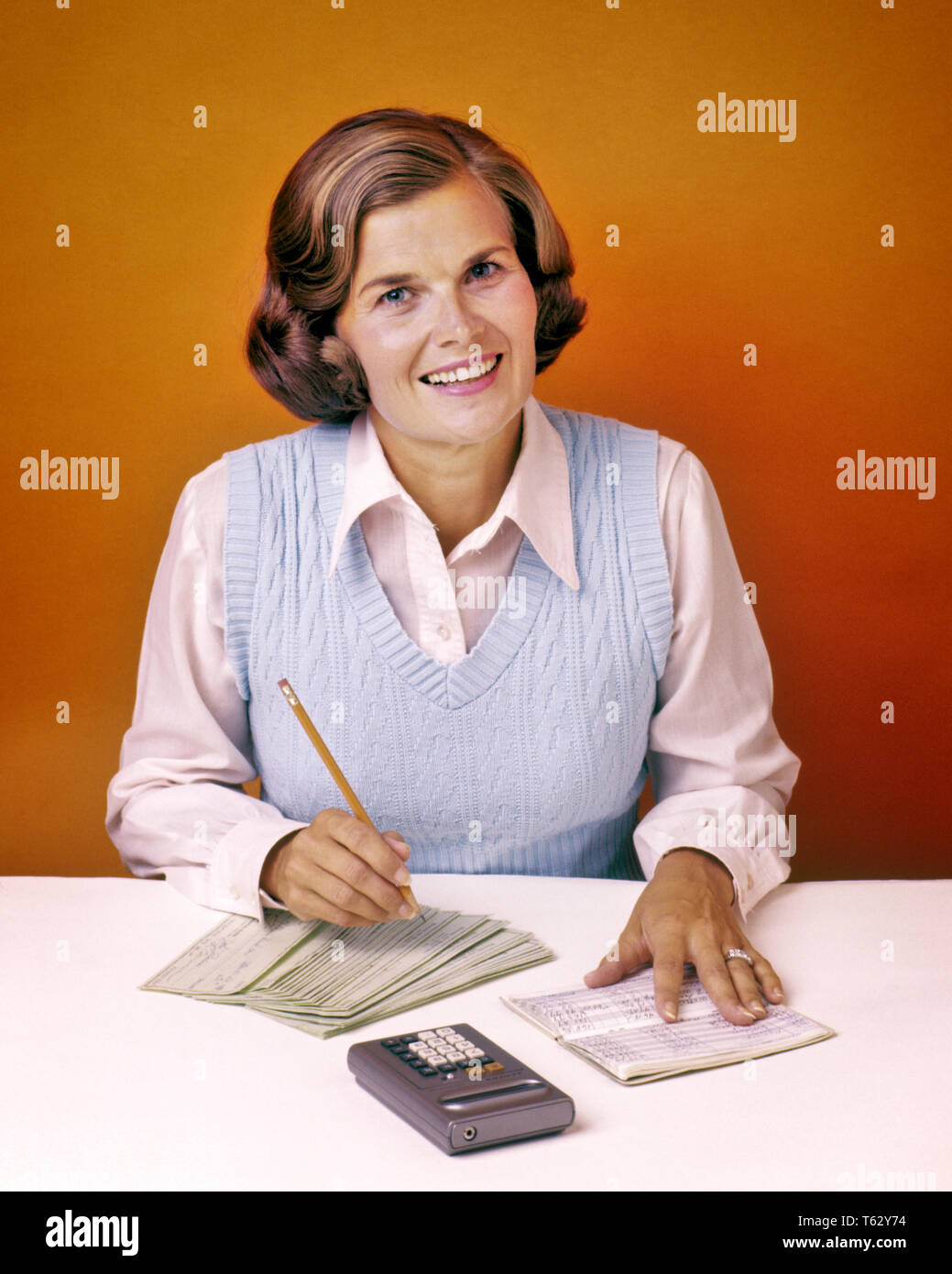 1970s SMILING WOMAN LOOKING AT CAMERA BALANCING HER CHECKBOOK USING CALCULATOR  - ks15032 BAN001 HARS EYE CONTACT GOALS HOMEMAKER HAPPINESS HOMEMAKERS CHEERFUL CHORE CHECKBOOK HOUSEWIVES OCCUPATIONS SMILES USING JOYFUL PERSONAL FINANCE MID-ADULT MID-ADULT WOMAN CAUCASIAN ETHNICITY OLD FASHIONED Stock Photo