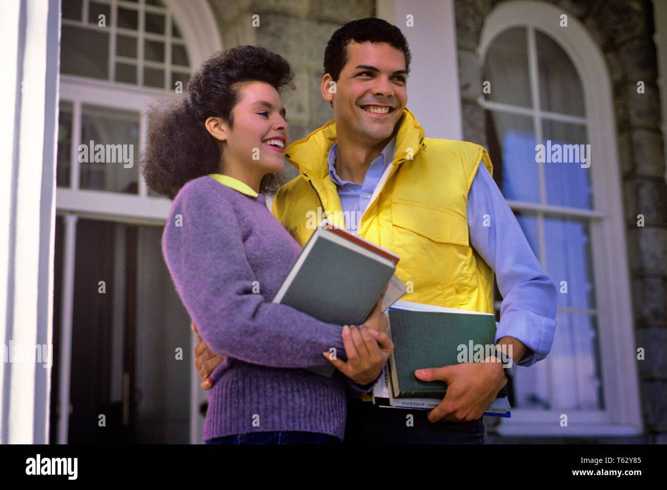 1980s SMILING AFRICAN AMERICAN COLLEGE COUPLE STANDING TOGETHER ON CAMPUS  - ks24462 DEG002 HARS ROMANCE BEAUTY SUBURBAN URBAN YELLOW COLOR OLD TIME BUSY FUTURE NOSTALGIA OLD FASHION 1 YOUNG ADULT TEAMWORK JOY LIFESTYLE CAMPUS FEMALES MARRIED SPOUSE HUSBANDS FRIENDSHIP HALF-LENGTH LADIES PERSONS RACIAL CARING MALES CONFIDENCE VEST GOALS SUCCESS PURPLE HAPPINESS STRENGTH UNIVERSITIES AFRICAN-AMERICANS AFRICAN-AMERICAN EXCITEMENT KNOWLEDGE LEADERSHIP PROGRESS BLACK ETHNICITY PRIDE ON OPPORTUNITY HIGHER EDUCATION CONCEPTUAL STYLISH COLLEGES COLLEGIATE HIGHER TOGETHERNESS WIVES YOUNG ADULT MAN Stock Photo