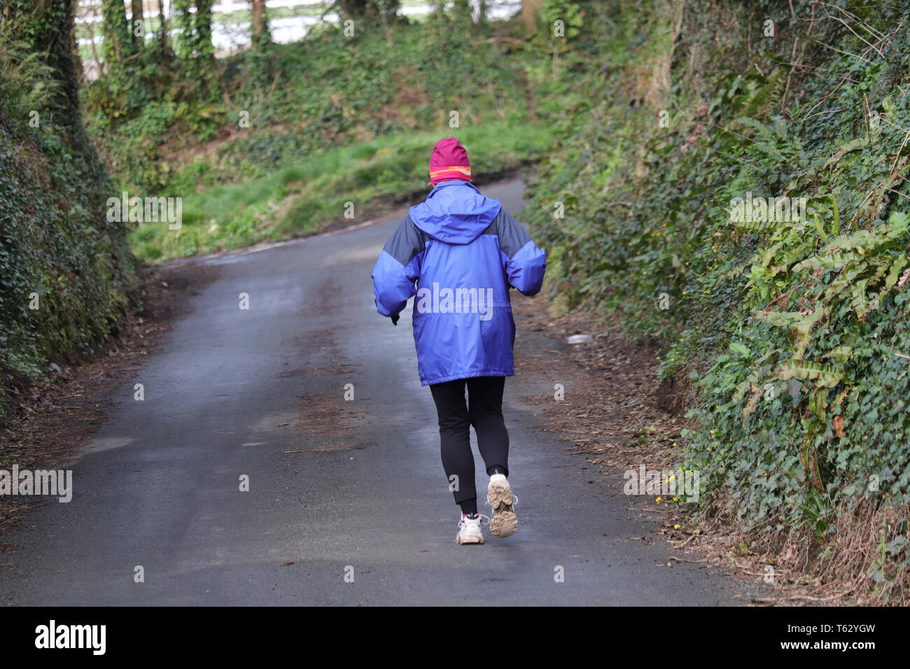 Single female in blue jacket running down country lane Stock Photo