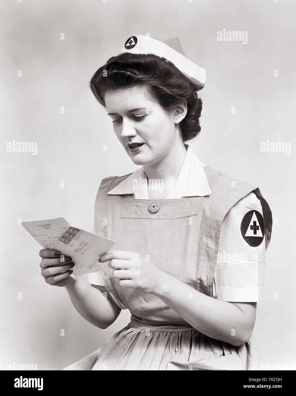 1940s WOMAN SERVING VOLUNTEER RED CROSS NURSE WEARING UNIFORM SMOCK DRESS AND CAP READING LETTER DURING WORLD WAR 2 - n445 HAR001 HARS CONFLICT FEMALES WW2 HEALTHINESS ILLNESS COPY SPACE HALF-LENGTH LADIES PHYSICAL FITNESS PERSONS INSPIRATION CARING RISK SPIRITUALITY CONFIDENCE EXPRESSIONS B&W CONCERNED BRUNETTE HEALTHCARE WELLNESS PREVENTION ADVENTURE STRENGTH HEALING COURAGE AND DIAGNOSIS WORLD WARS WORLD WAR WORLD WAR TWO HEALTH CARE WORLD WAR II IMPAIRMENT OCCUPATIONS TREATMENT CONNECTION CONCEPTUAL RED CROSS SMOCK STYLISH WORLD WAR 2 RELAXATION YOUNG ADULT WOMAN BLACK AND WHITE Stock Photo