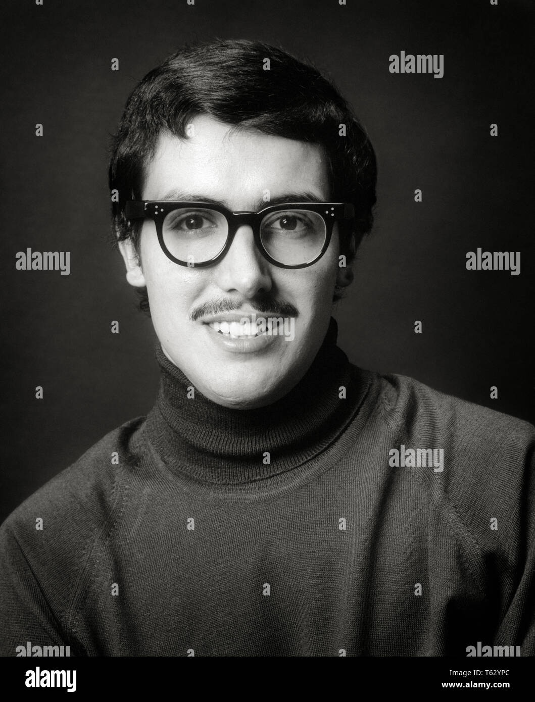 1970s PORTRAIT SMILING DARK HAIR MAN WITH THIN MUSTACHE LARGE BLACK PLASTIC FRAME GLASSES TURTLENECK SWEATER LOOKING AT CAMERA - o4053 HAR001 HARS HOME LIFE COPY SPACE PERSONS MALES CONFIDENCE EXPRESSIONS B&W EYE CONTACT MUSTACHE HEAD AND SHOULDERS CHEERFUL MUSTACHES UNIVERSITIES FACIAL HAIR SMILES HIGHER EDUCATION JOYFUL STYLISH COLLEGES BLAND INTENSE YOUNG ADULT MAN BLACK AND WHITE CAUCASIAN ETHNICITY HAR001 OLD FASHIONED TURTLENECK Stock Photo