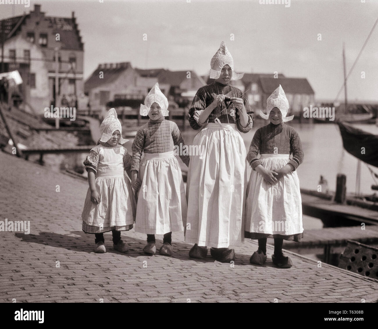 1920s MOTHER AND THREE DAUGHTERS TYPICAL DUTCH COSTUMES LOOKING AT CAMERA  WOODEN SHOES APRONS LACE CAPS VOLENDAM HARBOR HOLLAND - r3730 HAR001 HARS  NOSTALGIA OLD FASHION SISTER 1 JUVENILE STYLE LIFESTYLE HISTORY