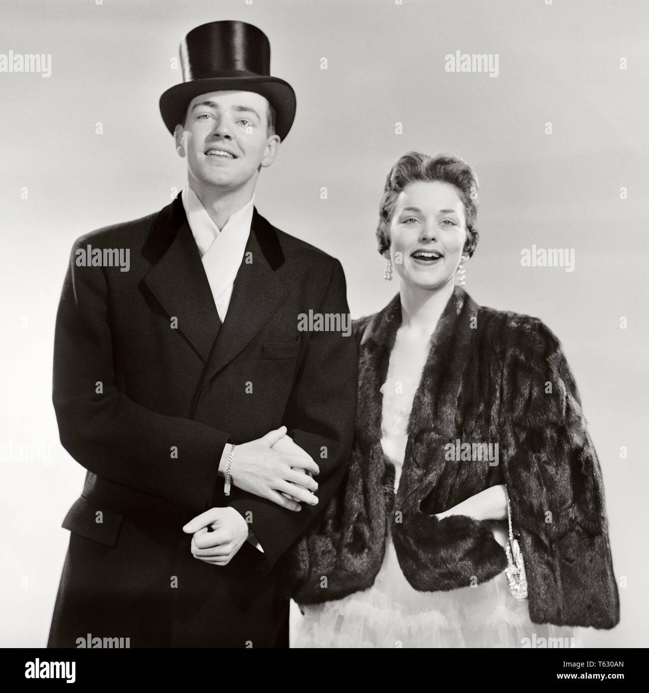 1950s MAN WOMAN ARM IN ARM DRESSED IN FORMAL CLOTHES MAN WEARING TOP HAT WOMAN FUR STOLE LOOKING AT CAMERA SMILING - r860 DEB001 HARS NOSTALGIA SILK OLD FASHION 1 GREETING FACIAL STYLE PLEASED JOY LIFESTYLE CELEBRATION FEMALES STUDIO SHOT COPY SPACE FRIENDSHIP HALF-LENGTH LADIES PERSONS MALES EXPRESSIONS B&W EYE CONTACT HAPPINESS CHEERFUL LEISURE STYLES SOPHISTICATED NIGHT ON THE TOWN SMILES UPSCALE STOLE COSMOPOLITAN JOYFUL STYLISH ATTIRE DEB001 DRESSED UP EVENING WARE FANCY DRESS FASHIONS MID-ADULT MID-ADULT MAN MID-ADULT WOMAN TOGETHERNESS TOP HAT BLACK AND WHITE CAUCASIAN ETHNICITY Stock Photo