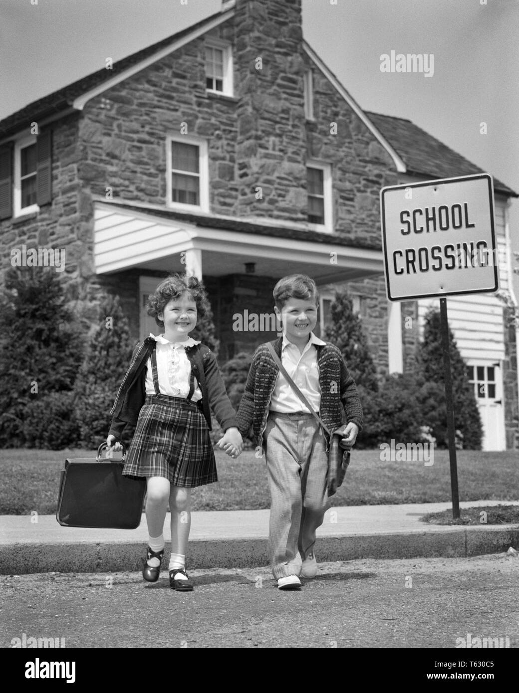 1950s YOUNG ELEMENTARY AGE BOY AND GIRL WITH BOOK BAGS HOLDING HANDS WALKING TOGETHER CROSSING SUBURBAN STREET GOING TO SCHOOL - s107 HAR001 HARS GOING AGE EXPRESSION OLD TIME NOSTALGIA BROTHER CROSS CROSSING OLD FASHION SISTER JUVENILE ELEMENTARY FACIAL STYLE FEAR SECURITY SAFETY TEAMWORK PLEASED JOY LIFESTYLE FEMALES BROTHERS HEALTHINESS HOME LIFE COPY SPACE FULL-LENGTH DANGER MALES SIBLINGS CONFIDENCE SISTERS EXPRESSIONS B&W SCHOOLS GRADE HAPPINESS CHEERFUL ADVENTURE STRATEGY AND EXCITEMENT MARY JANE TO PLAID SKIRT PRIMARY SIBLING SMILES CONCEPTUAL JOYFUL STYLISH K-12 CAUTION GRADE SCHOOL Stock Photo