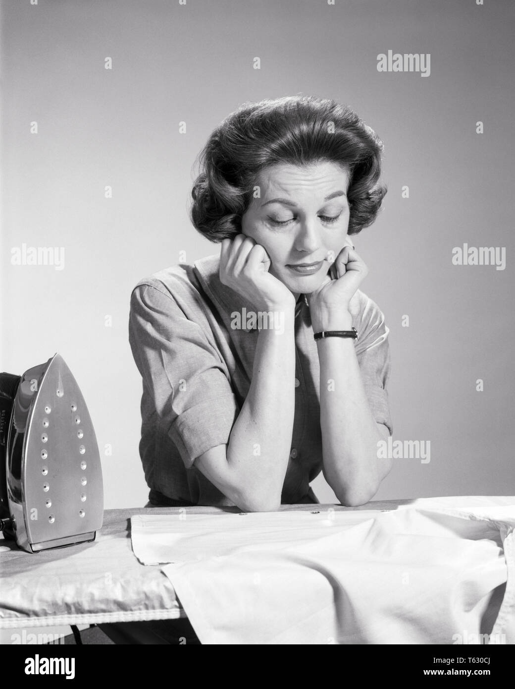 1960s TIRED HOUSEWIFE RESTING HER HEAD ON HANDS  ELBOWS ON IRONING BOARD TAKING A BREAK FROM IRONING EYES CLOSED   - s11592 HAR001 HARS STUDIO SHOT MOODY RURAL HOME LIFE WRISTWATCH COPY SPACE HALF-LENGTH LADIES PERSONS CARING TROUBLED B&W BREAK RESTING SADNESS BRUNETTE HOMEMAKER OVERWORKED HOMEMAKERS CHORE NAPPING HOUSEWIVES MOOD OCCUPATIONS ELBOWS TASKS CONCEPTUAL GLUM MID-ADULT MAN MID-ADULT WOMAN MISERABLE NAP RELAXATION STEAM IRON BLACK AND WHITE BOREDOM CAUCASIAN ETHNICITY HAR001 OLD FASHIONED TIREDNESS WEARY Stock Photo