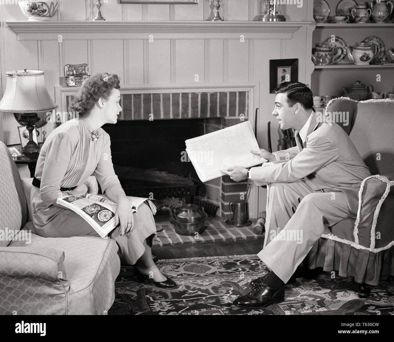 1950s COUPLE SITTING IN COMFORTABLE SUBURBAN LIVING ROOM HUSBAND POINTING OUT NEWSPAPER ARTICLE TO INTERESTED WIFE - s1193 HAR001 HARS LIFESTYLE FEMALES MARRIED SPOUSE HUSBANDS HOME LIFE COMMUNICATING FULL-LENGTH LADIES PERSONS CARING MALES B&W DISCUSSING LEISURE LIVING ROOM COMFORTABLE EXCITEMENT IN TO CONNECTION CONCEPTUAL CURIOUS STYLISH COMMENTING INTERESTED PERSONAL ATTACHMENT AFFECTION COOPERATION EMOTION MID-ADULT MID-ADULT MAN MID-ADULT WOMAN RELAXATION TOGETHERNESS WIVES BLACK AND WHITE CAUCASIAN ETHNICITY HAR001 OLD FASHIONED Stock Photo