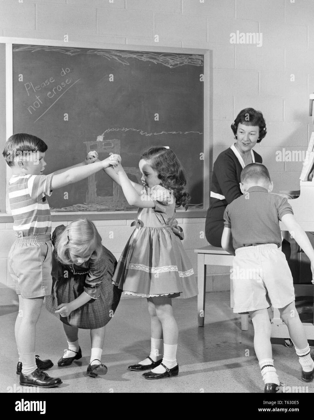 1950s 1960s SMILING WOMAN TEACHER PLAYING PIANO WHILE CHILDERN KINDERGARTEN STUDENTS DANCE AND PLAY - s13150 HAR001 HARS 1 JUVENILE TEACHERS LIFESTYLE SOUND FIVE MUSICIAN FEMALES 5 HEALTHINESS COPY SPACE FRIENDSHIP FULL-LENGTH HALF-LENGTH LADIES PHYSICAL FITNESS PERSONS DOING MALES B&W HAPPINESS KINDERGARTEN INSTRUCTOR MARY JANE OCCUPATIONS MUSICAL INSTRUMENT CONNECTION EDUCATOR IMAGINATION PLAYS COOPERATION EDUCATING EDUCATORS INSTRUCTORS JUVENILES MID-ADULT MID-ADULT WOMAN SCHOOL TEACHES BLACK AND WHITE CAUCASIAN ETHNICITY HAR001 OLD FASHIONED Stock Photo