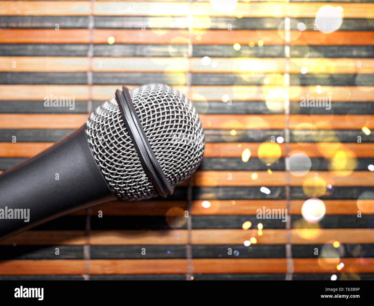 Top-Down View of a Microphone Head on a Striped Yellow and Black Bamboo Mat Background. Round Golden Celebration Soft Lights. Karaoke Bar, Holiday, Fe Stock Photo