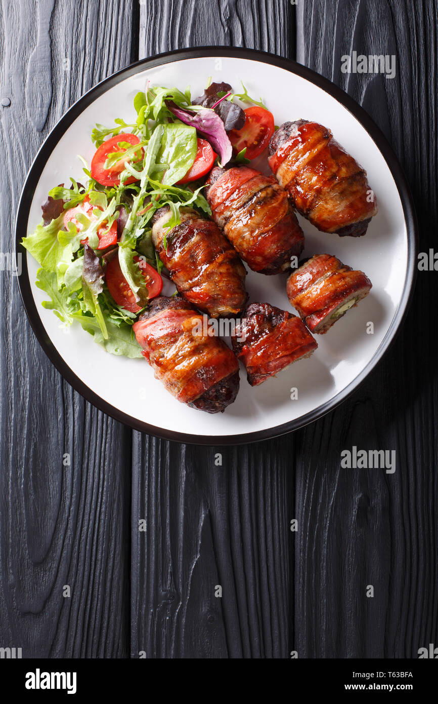 Delicious Armadillo eggs stuffed with jalapeno and cheese wrapped in bacon served with fresh salad close-up on a plate on the table. Vertical top view Stock Photo