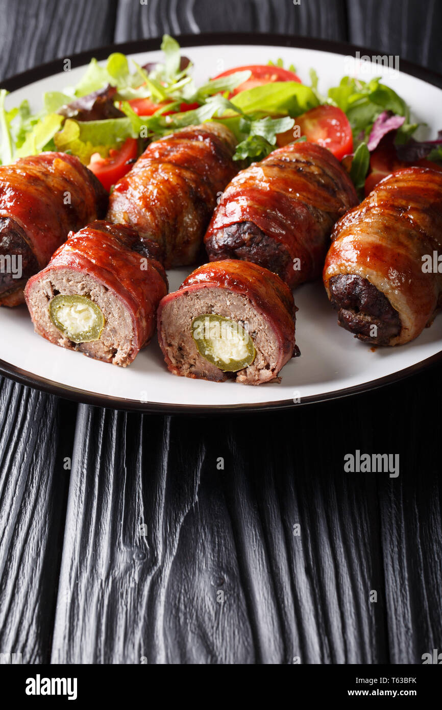 Smoked Armadillo eggs with jalapeno and cheese wrapped in bacon served with fresh salad close-up on a plate on the table. vertical Stock Photo