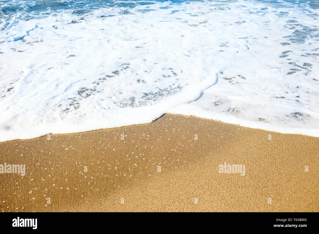Sandy beach and soft blue ocean wave with white foam. Stock Photo