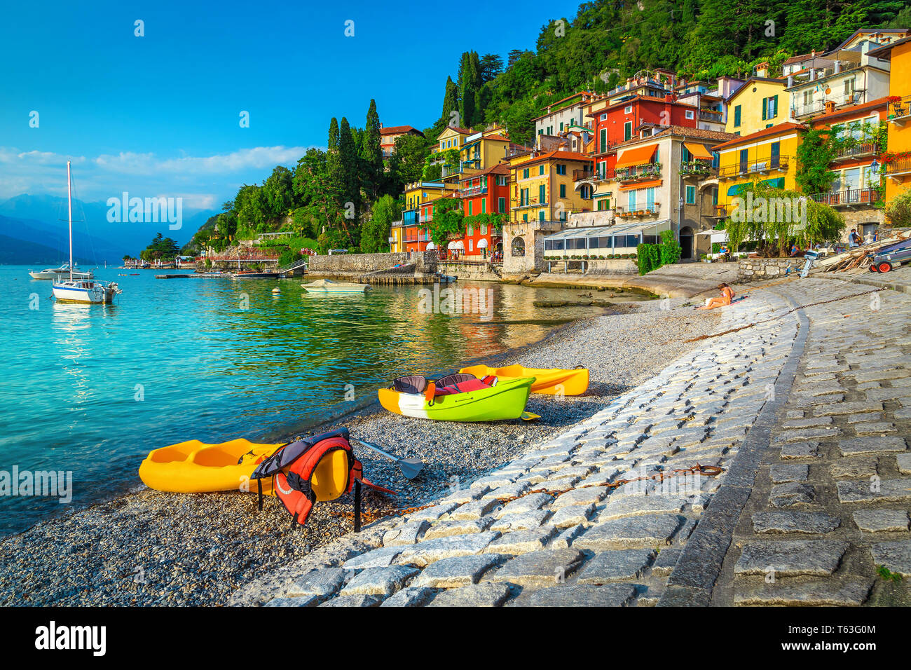 Famous travel and tourism location with colorful buildings. Summer holiday resort with colorful canoes, kayaks and boats, Varenna, lake Como, Italy, E Stock Photo