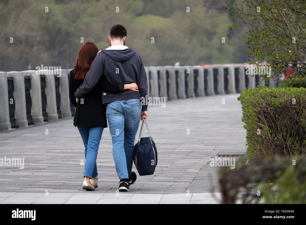 Couple in love hugging and walking in a park, rear view. Embracing guy and girl on romantic date, people in jeans, relationship, real feelings Stock Photo