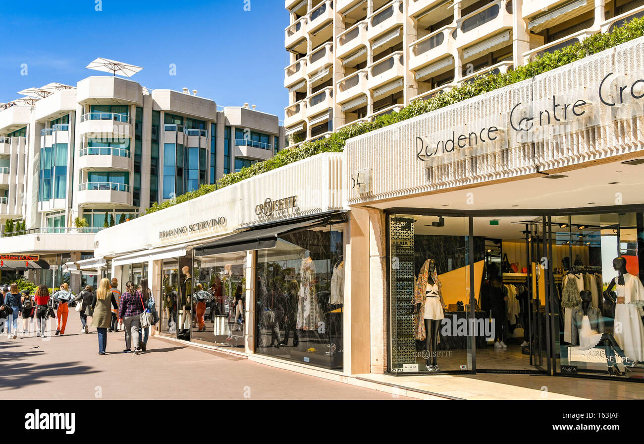 CANNES, FRANCE - APRIL 2019: People walking past designer shops on the seafront in Cannes. Stock Photo