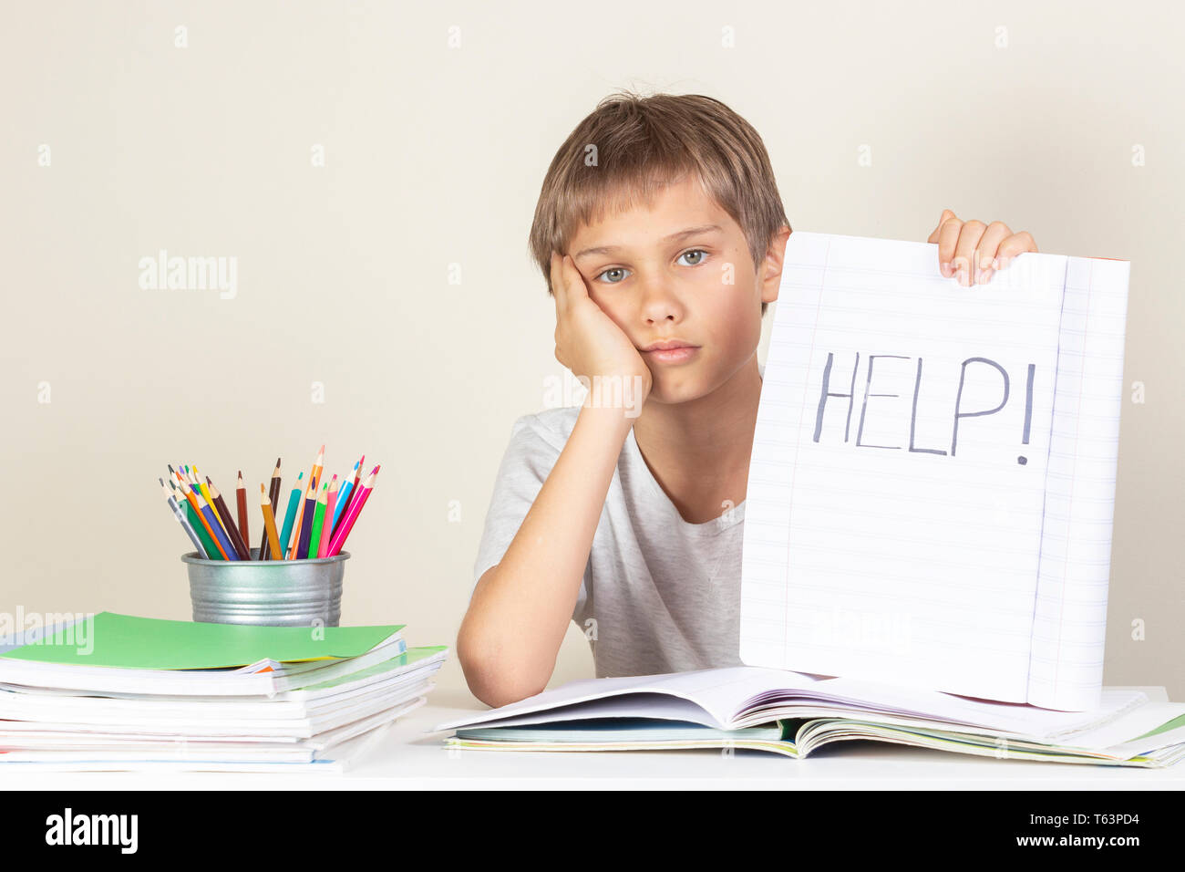 Help sign. Sad tired unhappy child doing homework and holding notebook