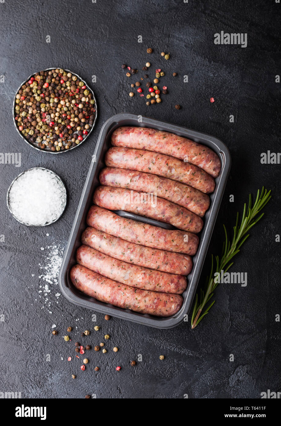 Raw beef and pork sausage in plastic tray with salt and pepper on black