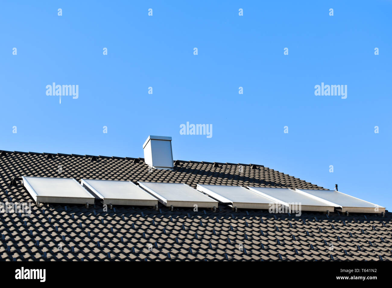 Hot water solar panels on dark house roof. Sunny day, bright blue sky ...