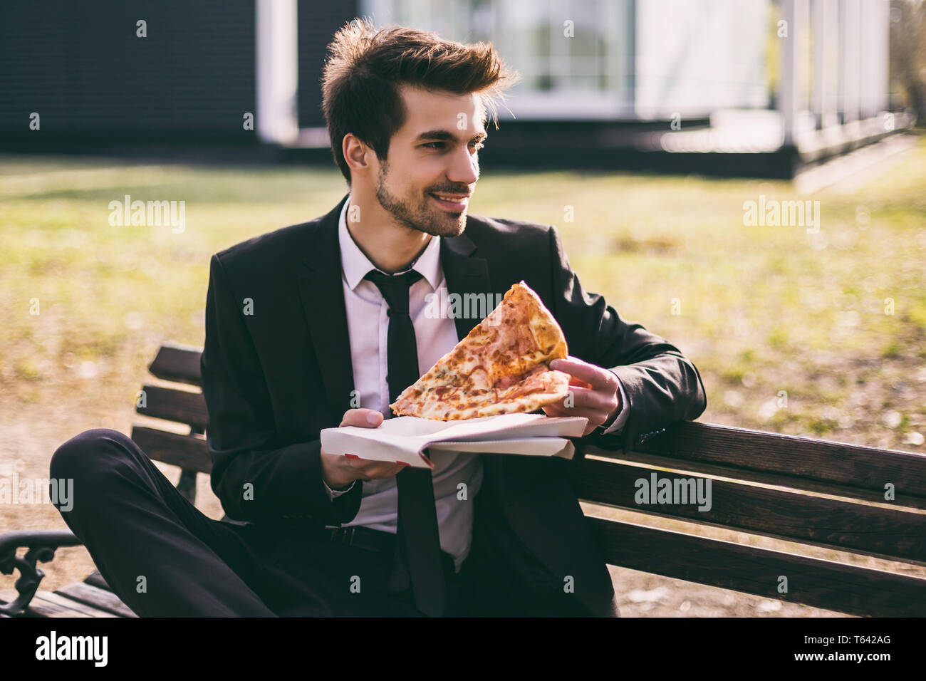 Elegant businessman enjoys eating pizza on his lunch break while sitting outdoor.Toned image. Stock Photo