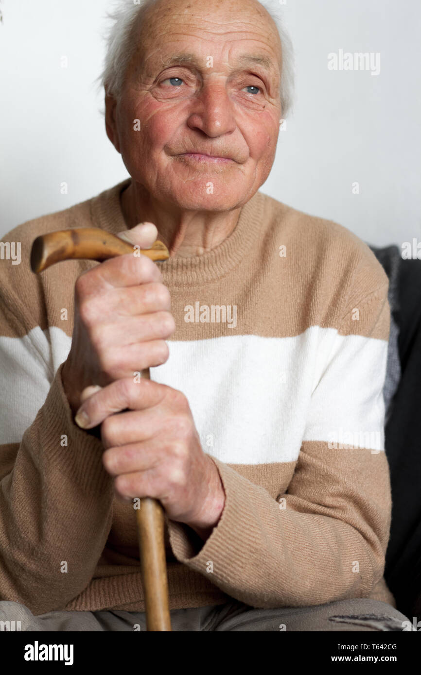 Portrait of a smiling old man who put his hands on the handle of a wooden cane, health at home. Stock Photo