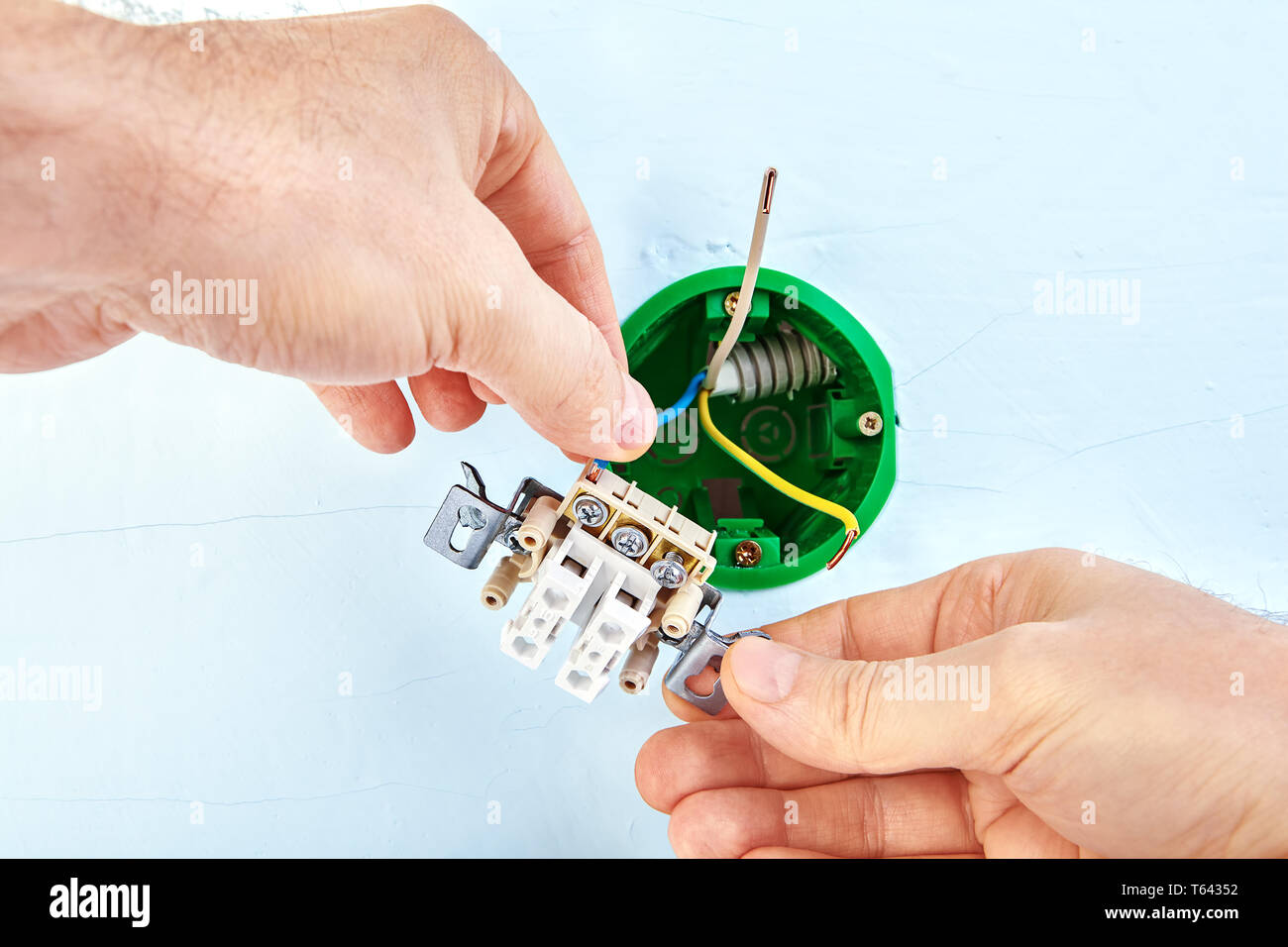 Electrician is mounting electrical socket box inside gypsum