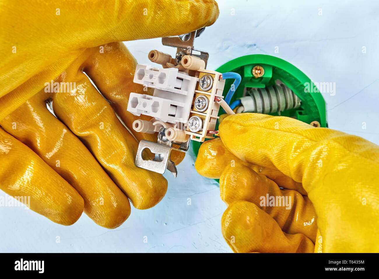 Electrician in yellow protective gloves is installing new light switch inside drywall. Stock Photo