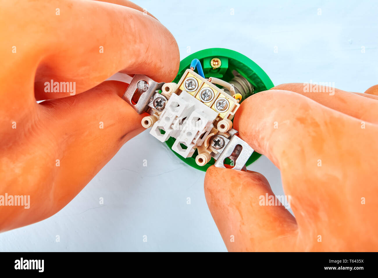 Electrician in protective gloves is installing double switch placed in the socket. Stock Photo