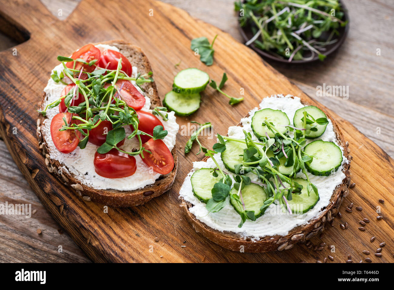 Healthy toasts with cream cheese, cucumber, cherry tomato and microgreen on wooden board. Appetizer or breakfast food Stock Photo