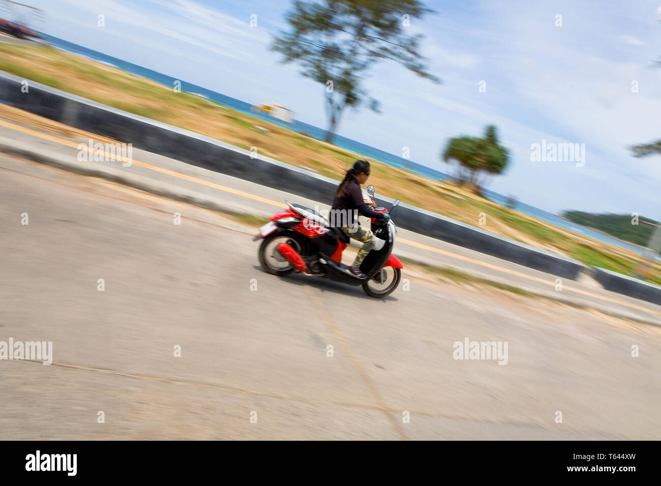 Karon, Thailand, February 20, 2018: East Asian woman riding at high speed on a scooter along the promenade. Dynamics and speed. Stock Photo