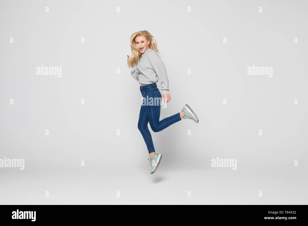 Full length portrait of a young woman jumping and celebrating over gray ...